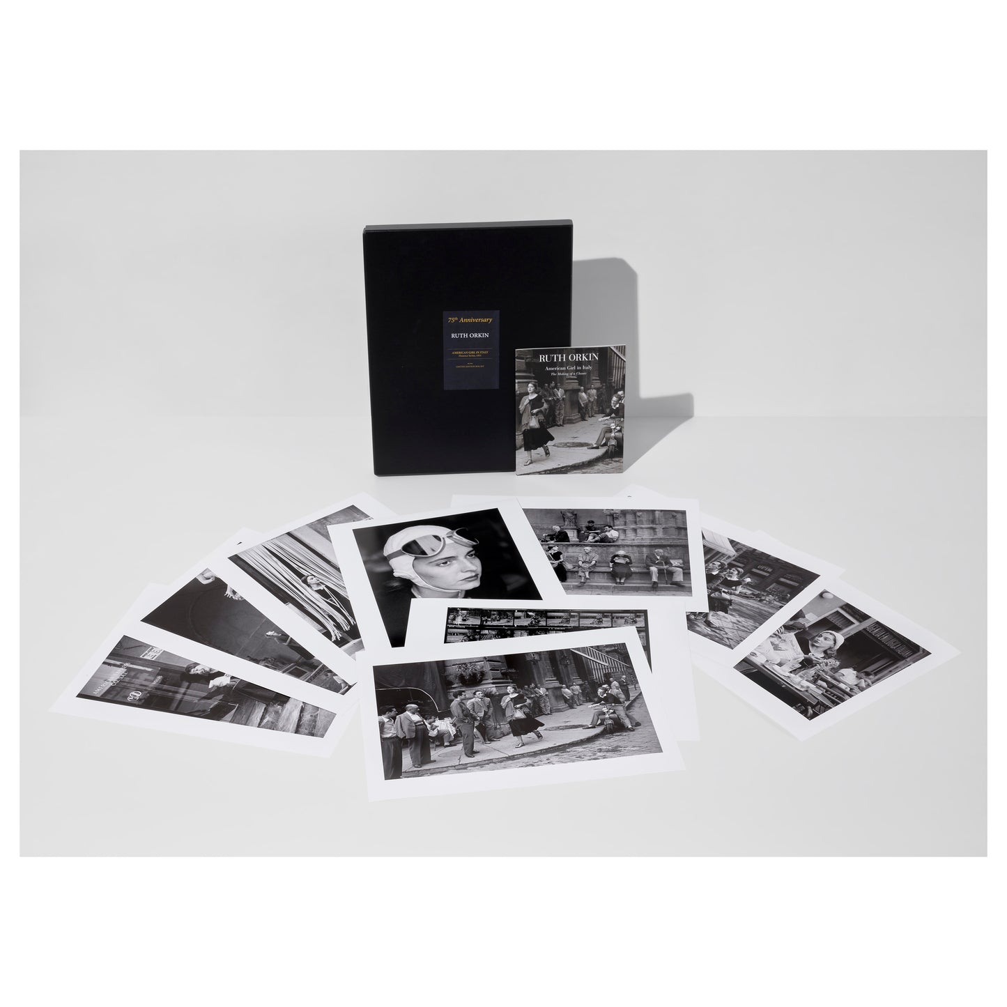 Collection of black and white Ruth Orkin photos from American Girl in Italy, a portfolio box, and an exhibition catalogue on a light gray background